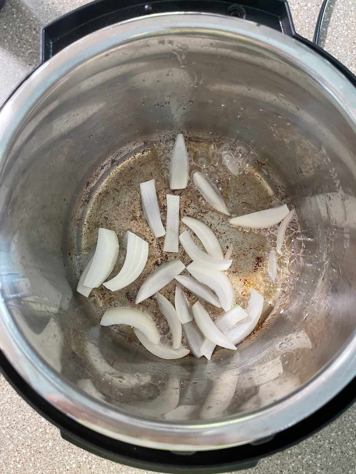 Sliced onions cooking in the bottom, of the pressure cooker with bacon fat.