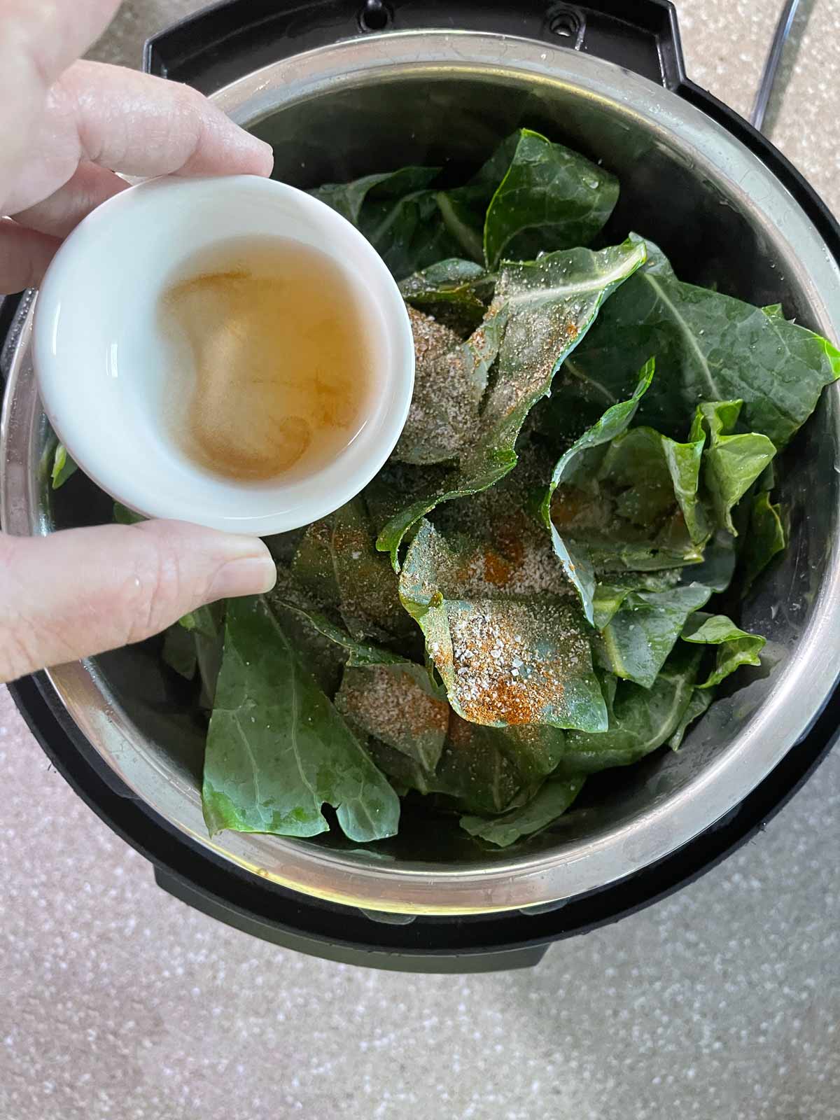 Chicken broth and apple cider vinegar are poured over collard greens.
