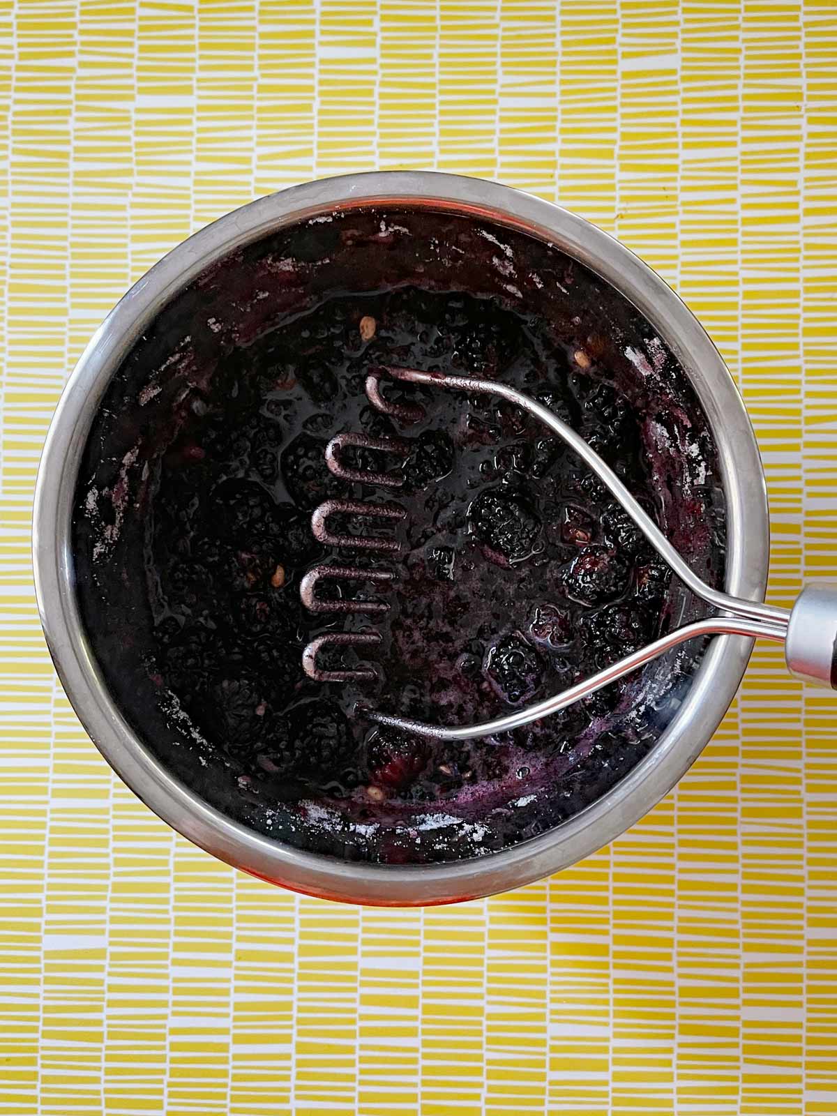 Image of blackberries being crushed with a potato masher.