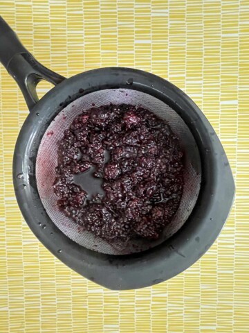 Image of the mixture being drained through a sieve over a bowl.