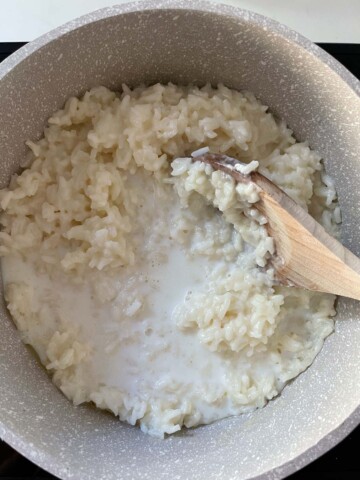 Stirring milk into cooked rice with a wooden spoon.
