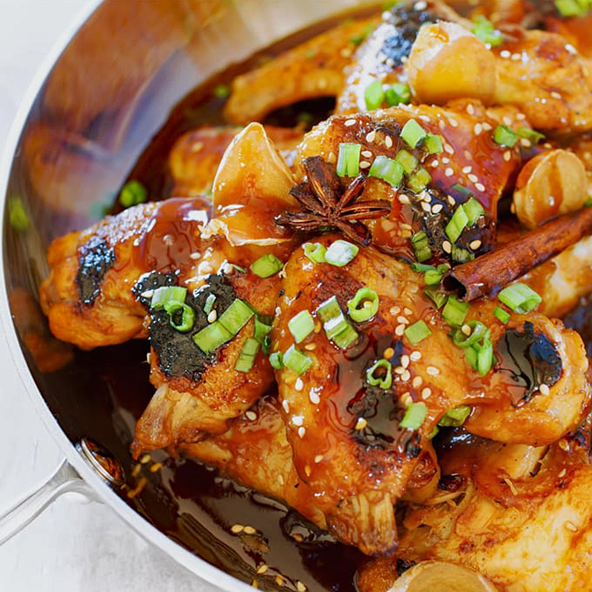 Chicken wings with sauce, scallions, and star anise in a pan.