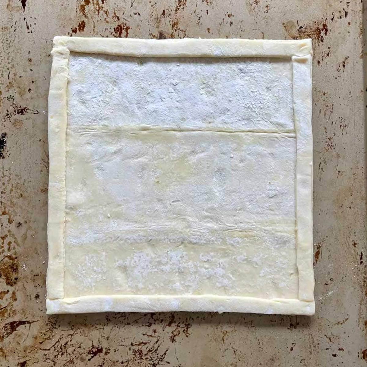 Square of puff pastry with raised edges on sheet pan.