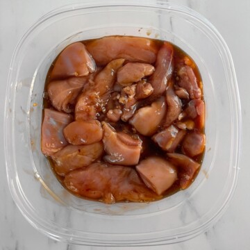 Chicken pieces marinating in a plastic container.