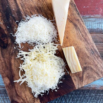 Cutting board with grated Gruyere cheese and Parmesan cheese.
