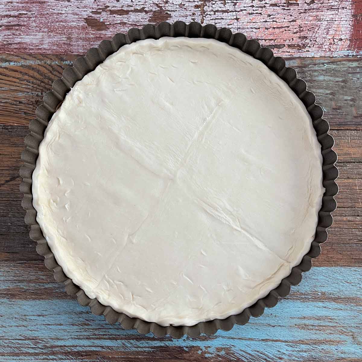 Tart pan with puff pastry placed on the parchment paper.