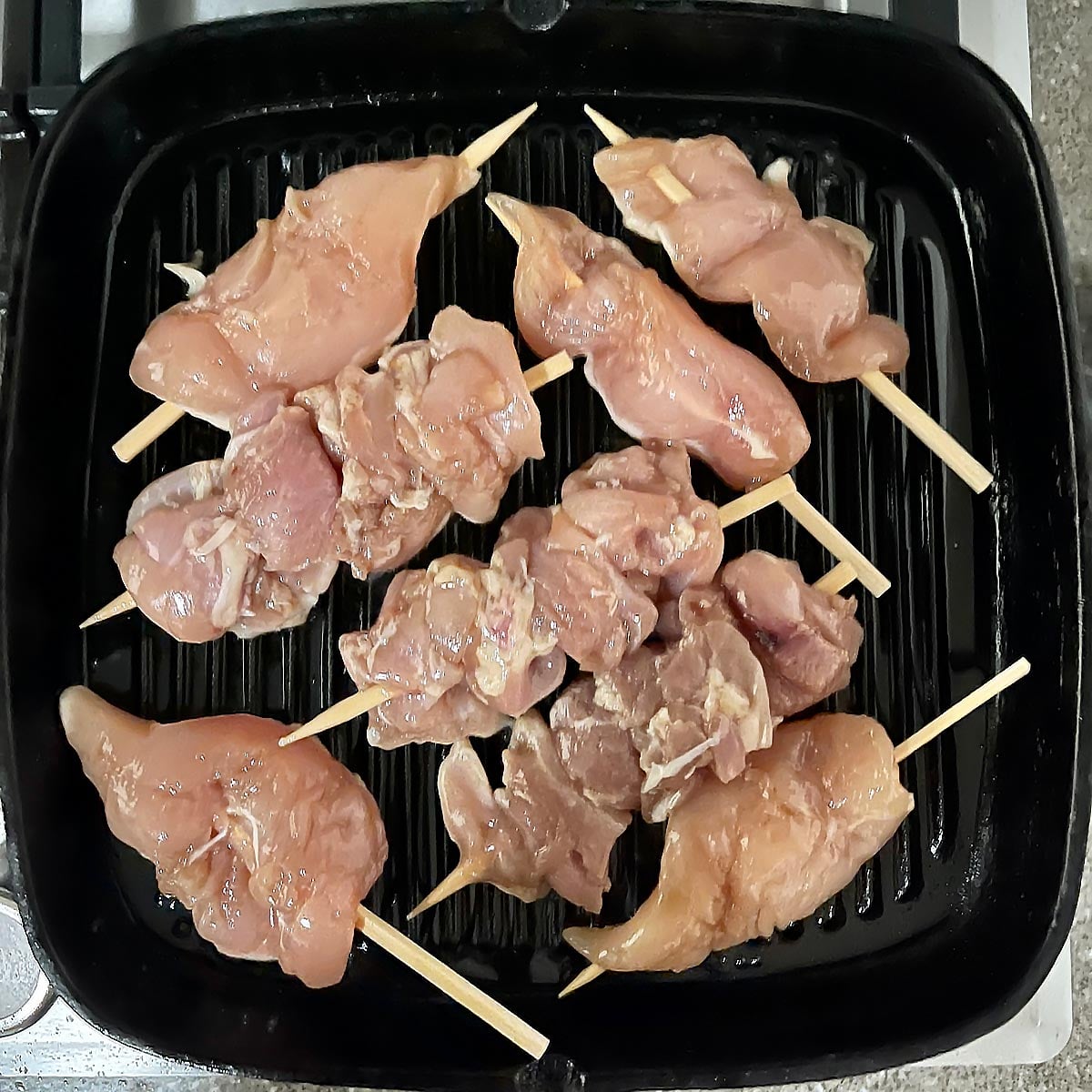 Raw chicken being placed on hot grill pan.