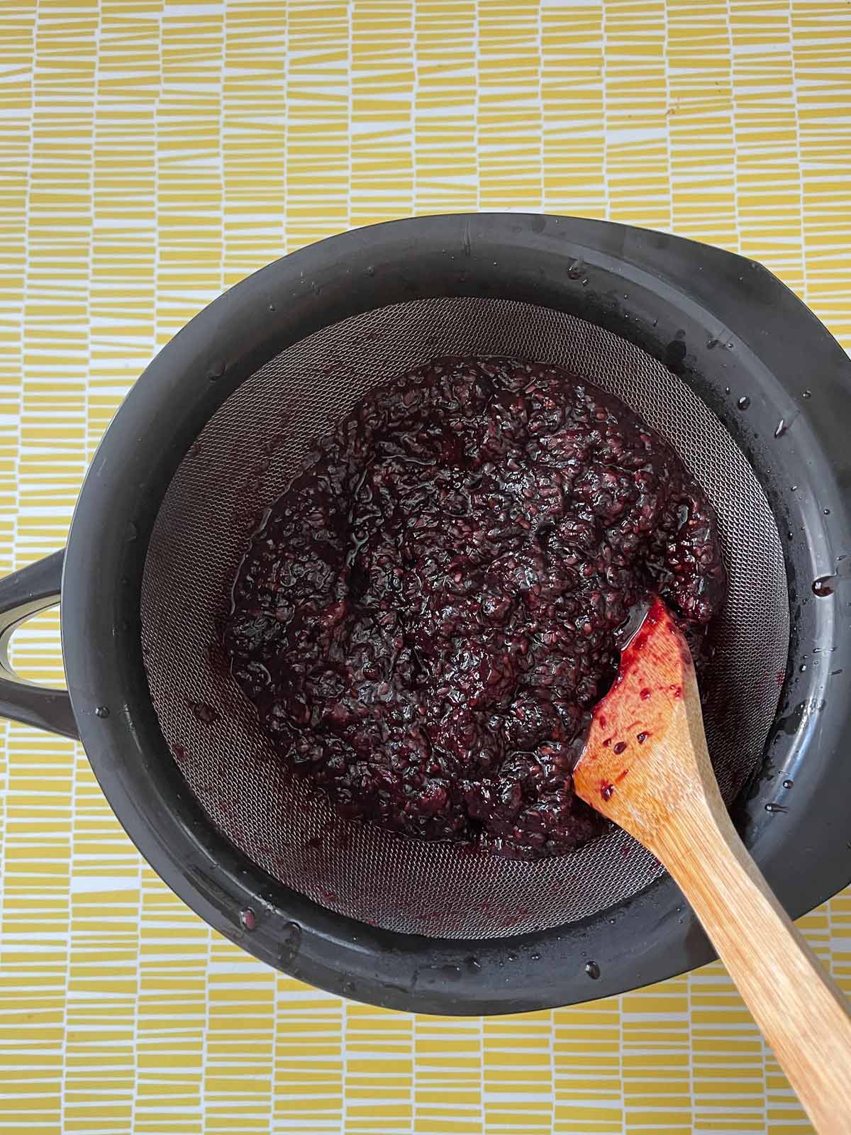 Image of the blackberry pulp being forced through the sieve with a wooden spoon.