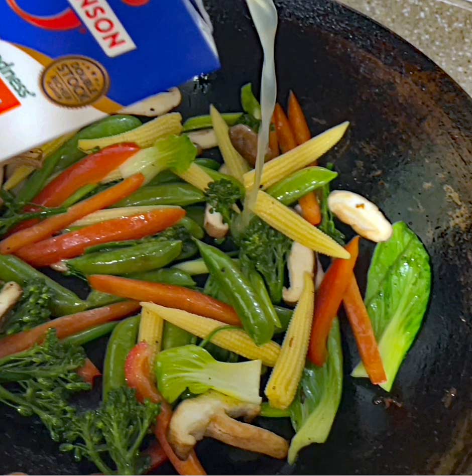 image of chicken broth being poured into the wok with the vegetables.