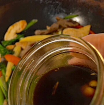 Image shows the stir fry sauce being poured into the hot wok with the meat and vegetable mixture.
