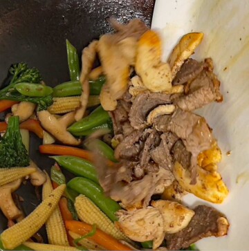 Image of the cooked meat being added back into the wok with the vegetables.