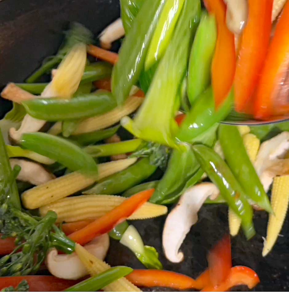 Image shows vegetables being stir fried with a spatula.