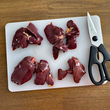 Untrimmed liver slices on cutting board with kitchen shears.