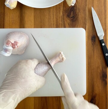 Raw chicken leg being cut around the diameter close the the bone end.