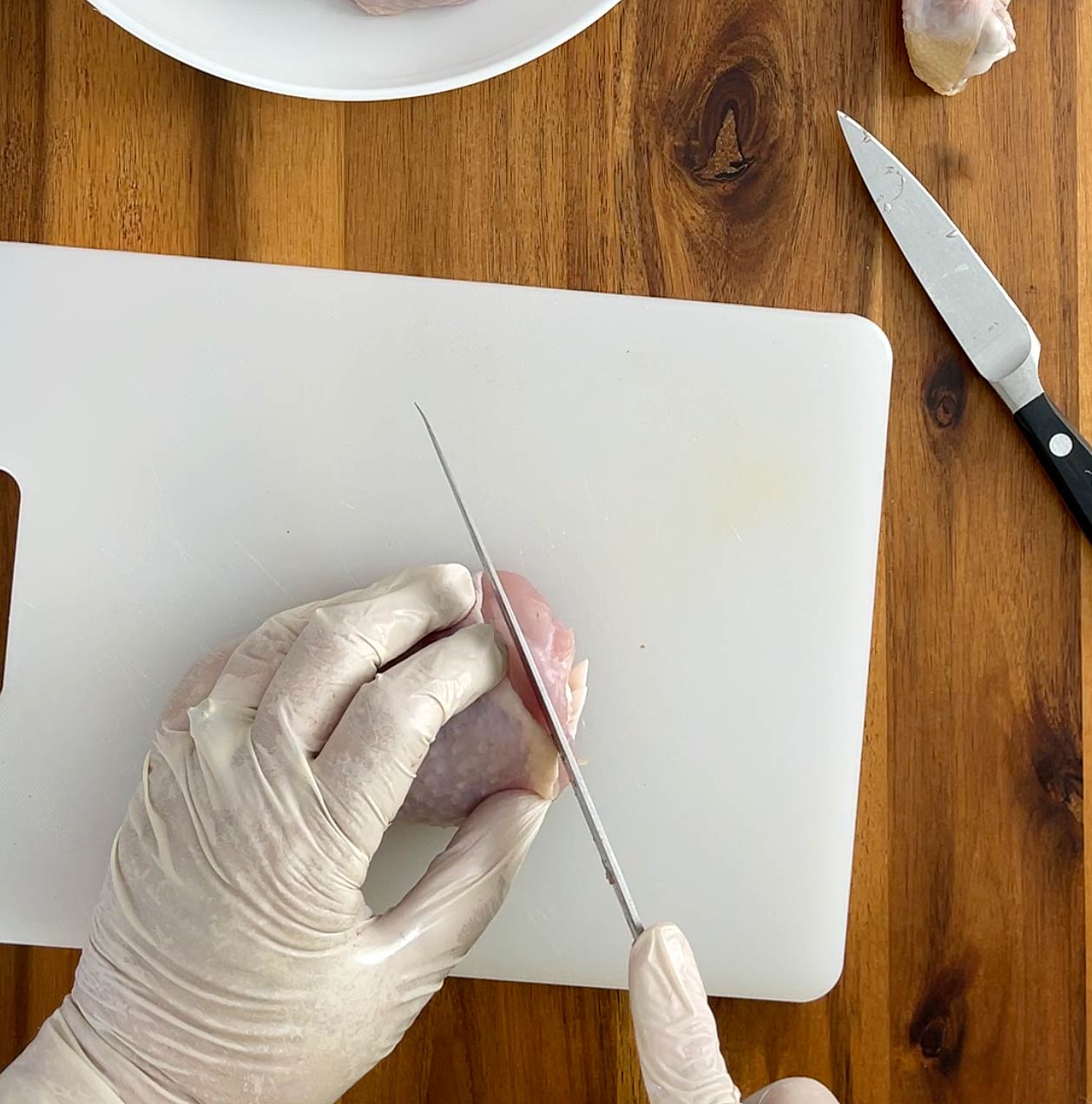Hands using a knife to cut a corner off of chicken leg.