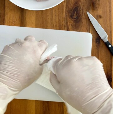Hands using paper towels to pull off cut chicken piece.