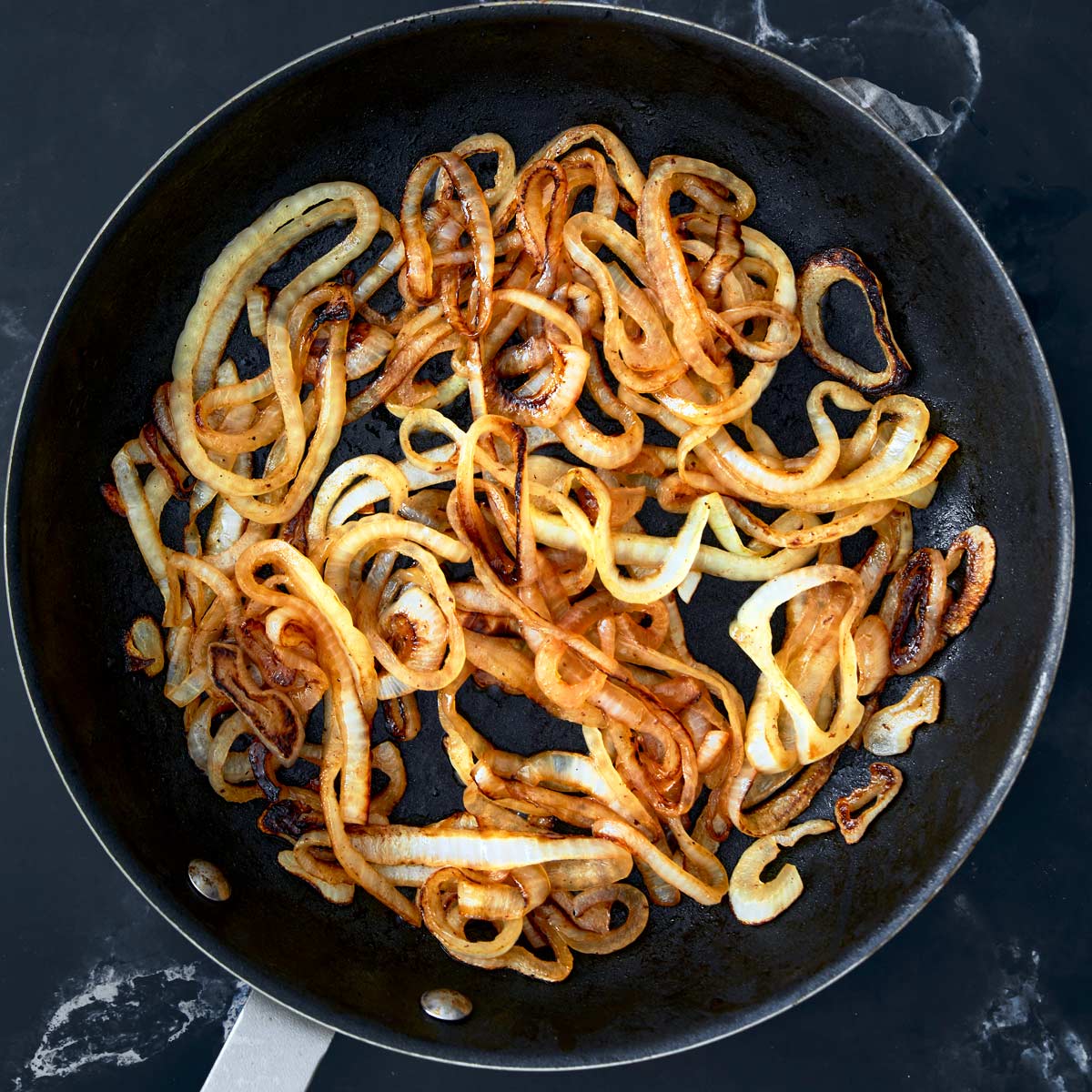 Large skillet with golden brown cooked sliced onion.