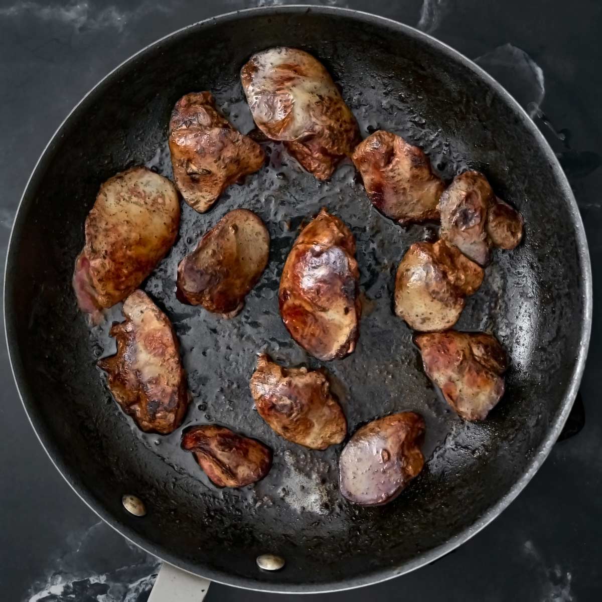 Skillet with chicken livers cooking on second side.