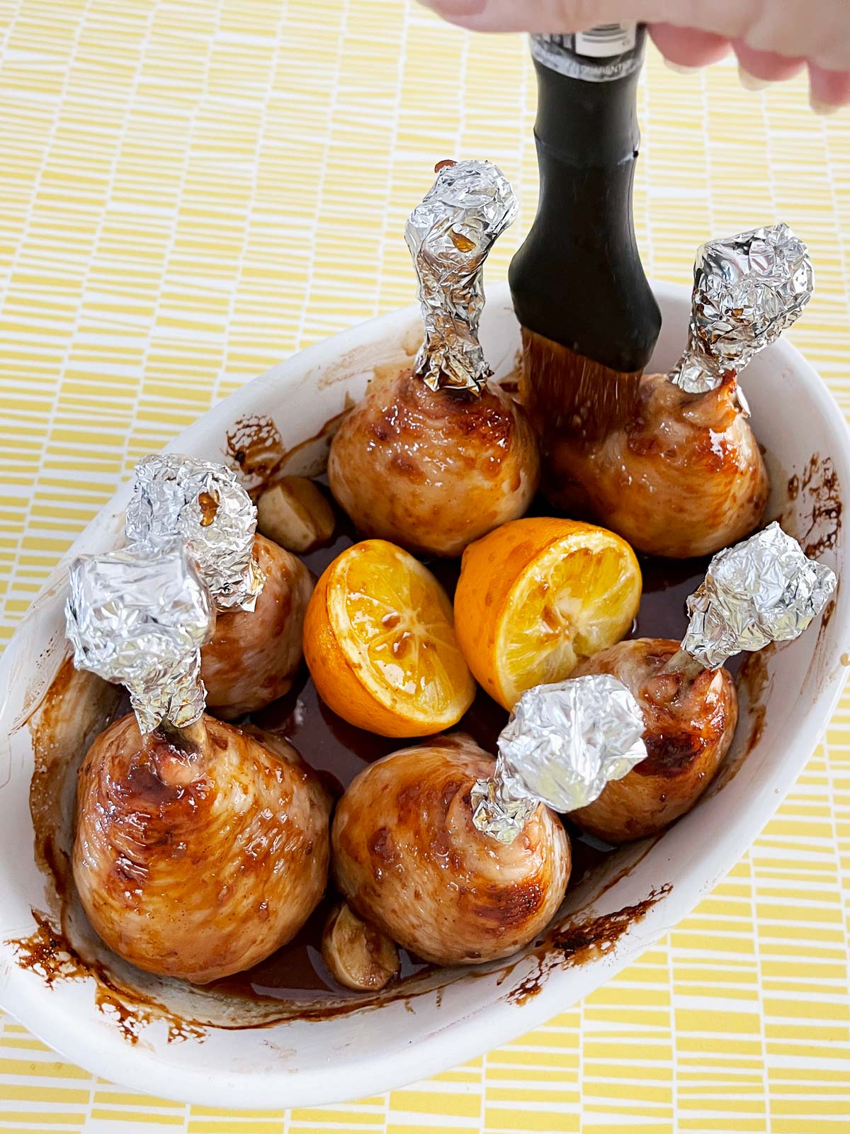 Basting chicken lollipops with BBQ sauce midway through cooking.