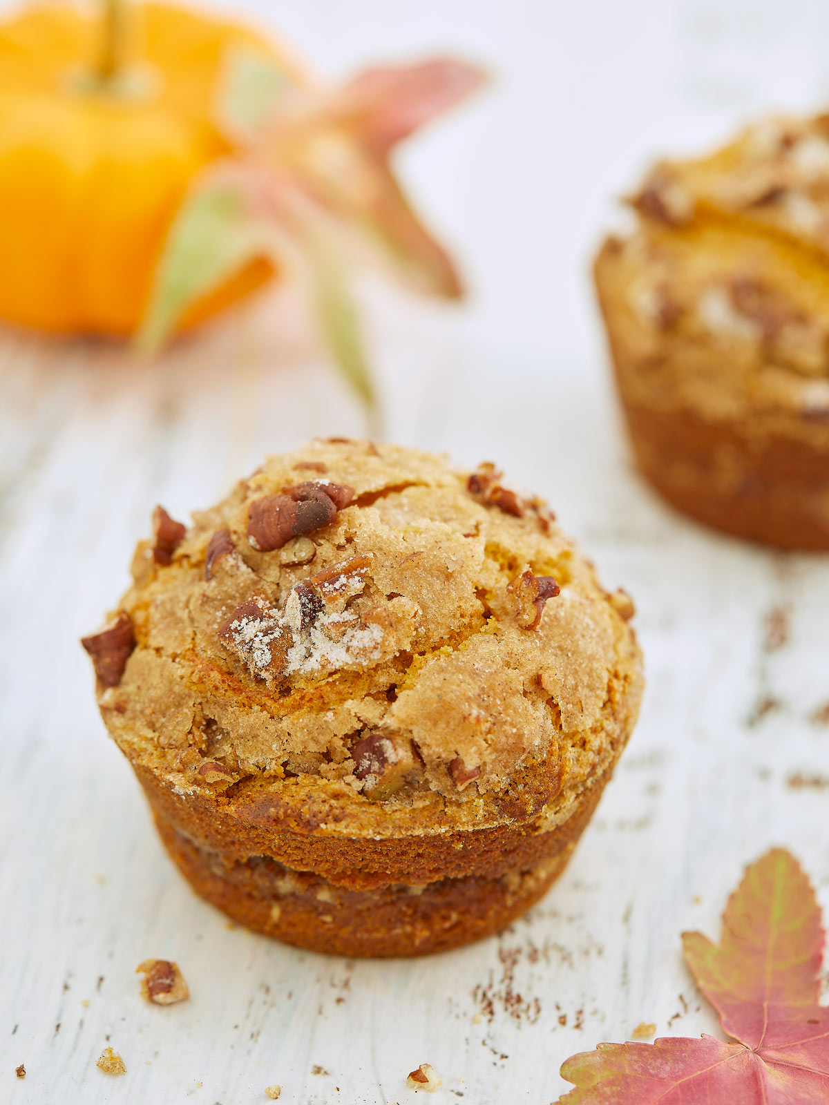 A muffin with sugar crackles on top on white wood board with pumpkin and autumn leaves.