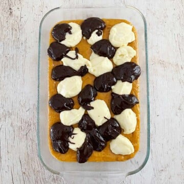 Baking dish with cake batter topped with alternating dollops of cream cheese mixture and chocolate.