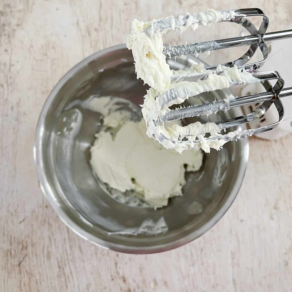 Mixing bowl with hand mixer beating cream cheese.