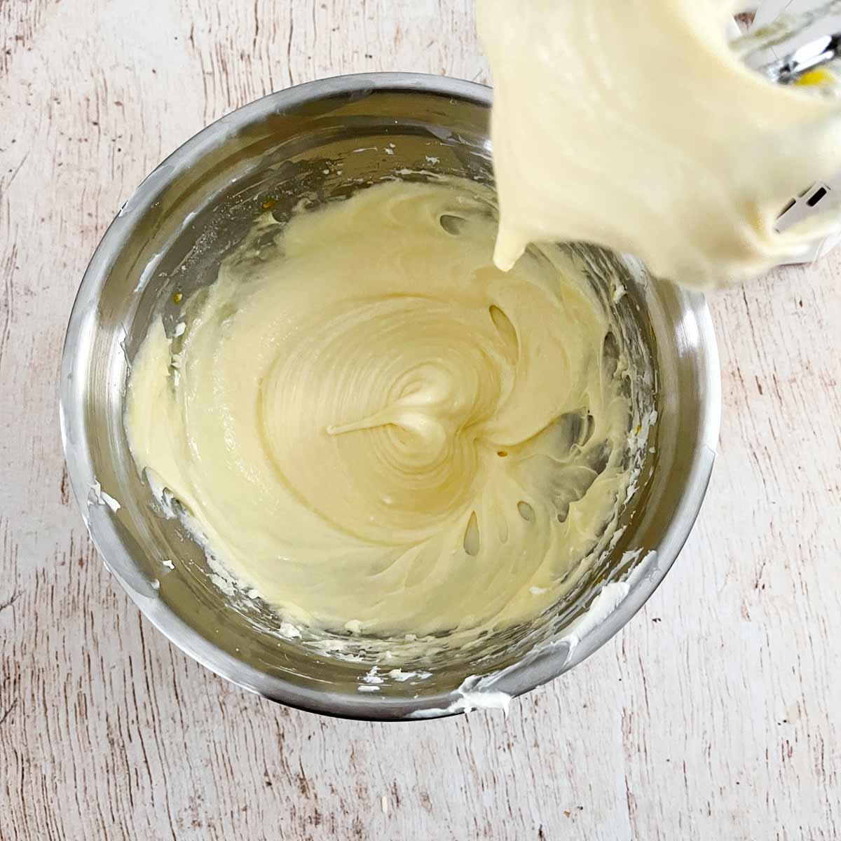 Mixing bowl with pale yellow beaten cream cheese mixture.
