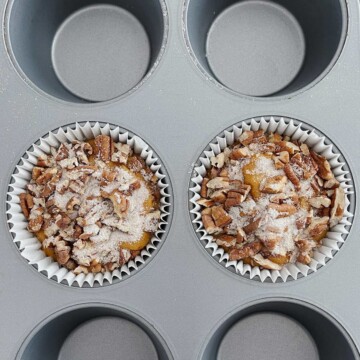 Baking tin with paper cupcake liners and batter topped with sugar cinnamon pecan mixture.