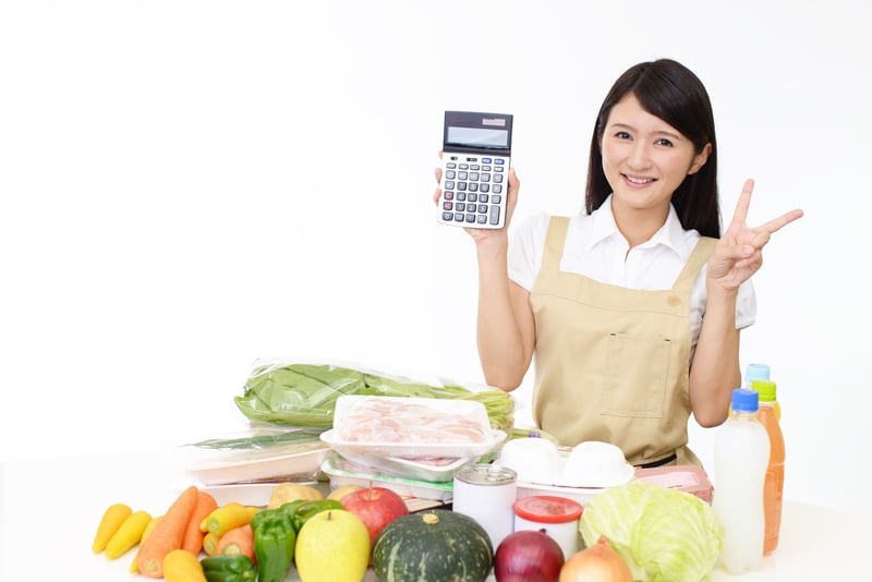 Young woman with calculator, groceries, making the peace sign. 