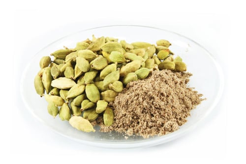 A plate with whole cardamom pods and ground cardamom.