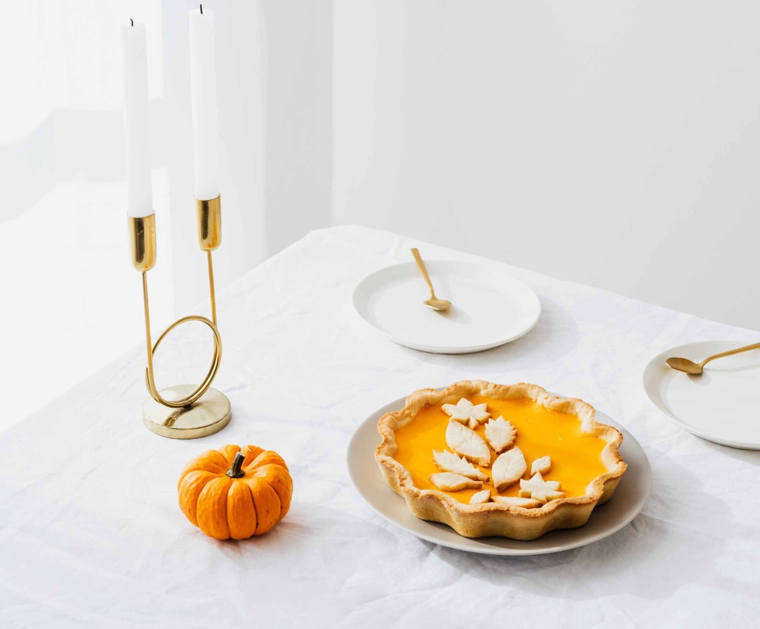 Small pumpkin pie with twp plates and gold candles.