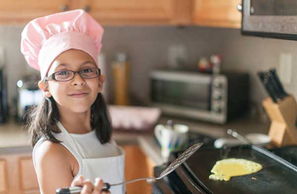 Little girl with a pink chef's hat making pancakes.