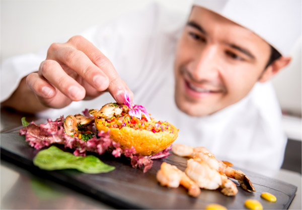 Young male chef garnishing a plate of food.