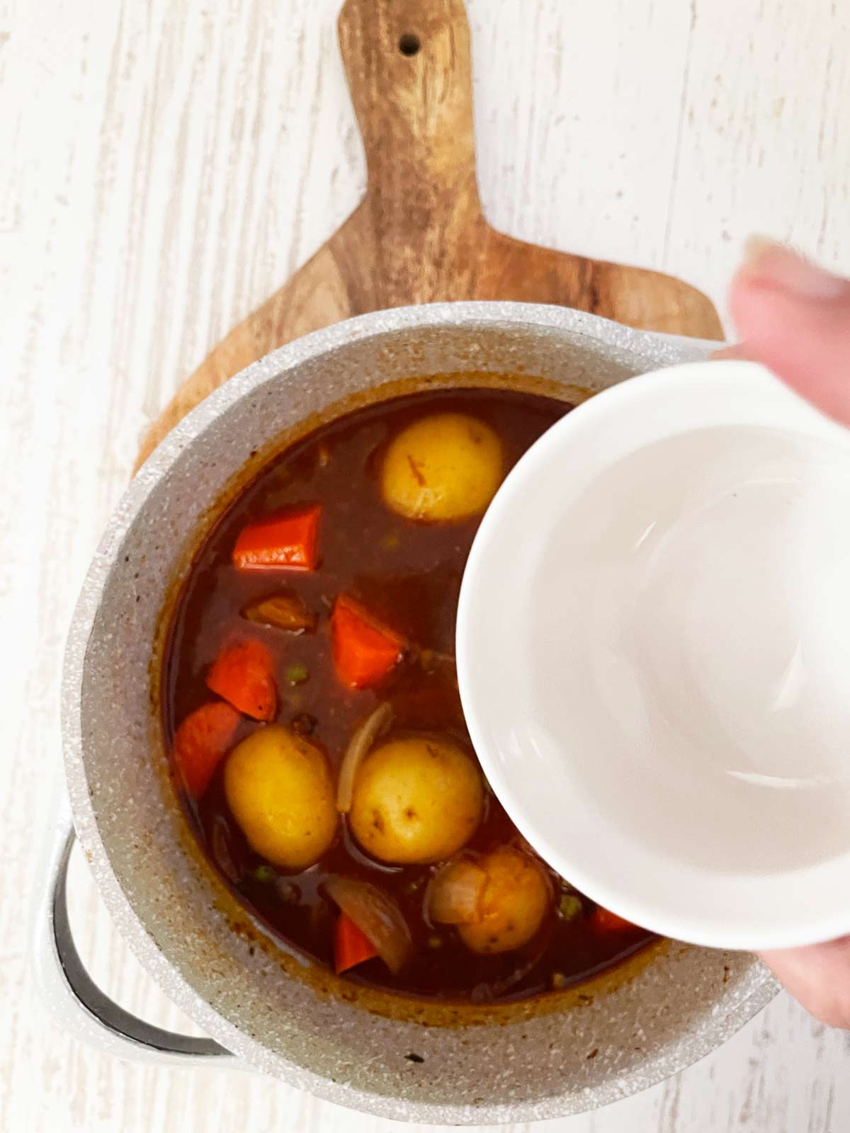 Cooked beef stew with cornstarch slurry being poured in for thickening the sauce/