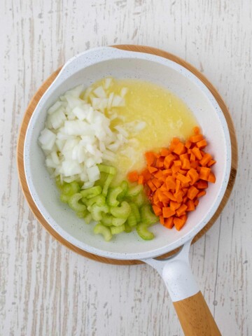 White skillet with melted butter diced celery, carrots, and onion.