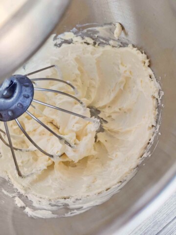 Butter and cream cheese are mixed in the bowl of a stand mixer with a whisk attachment.