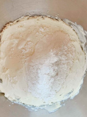 Powdered sugar is added to the mixing bowl with the creamy butter confectioners sugar mixture.