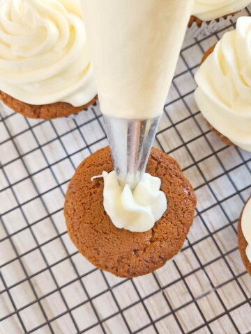Frosting is being piped on a gingerbread cupcake using a piping bag and tip.