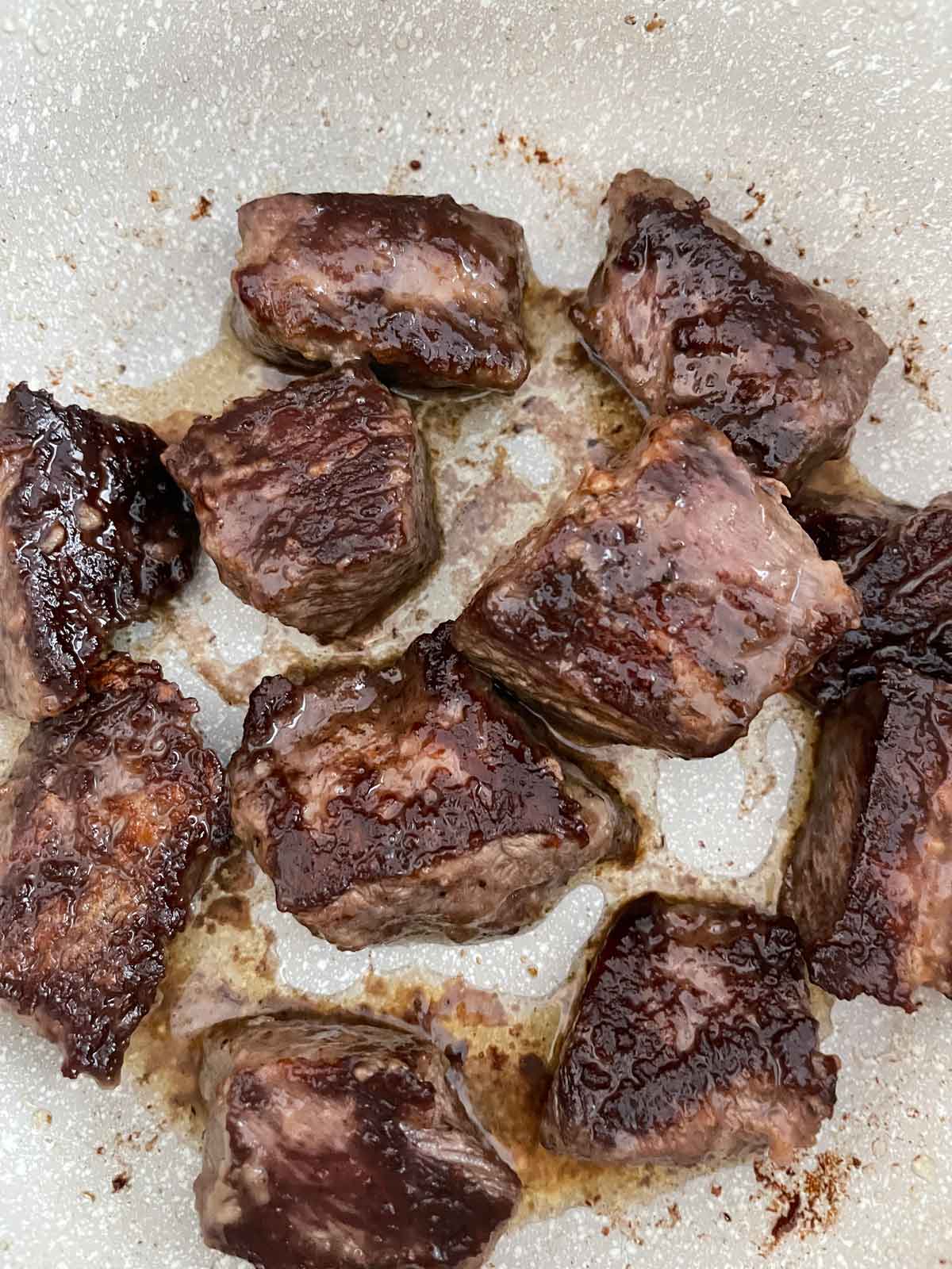 A Close-up of the seared beef chuck shows the browned bits on the bottom of the pan.