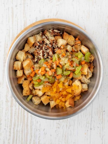 Large bowl with cubed bread, diced apricots, pecans, and cooked vegetables, and butter.