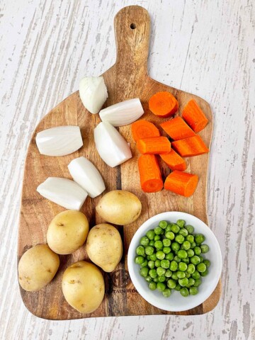 Whole small white potatoes, small onion cut into six wedges, peeled carrots cut into 1" cubes, and a small plate of frozen peas.