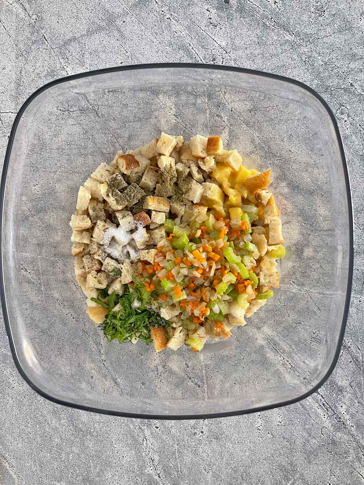 Large clear bowl with Bread cubes, herbs, seasonings, and cooked vegetables.