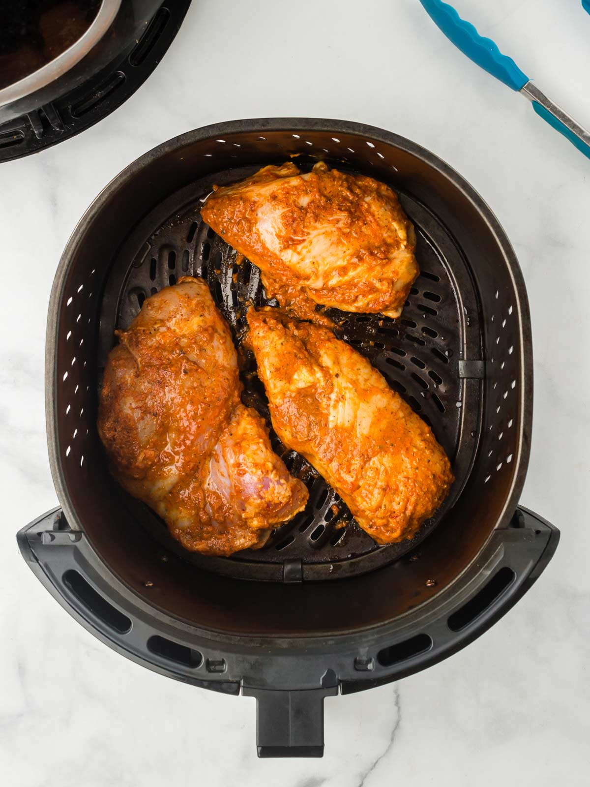 Uncooked chicken in the basket of an air fryer.