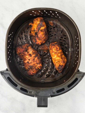 Golden brown pieces of chicken in an air fryer basket with charred edges.