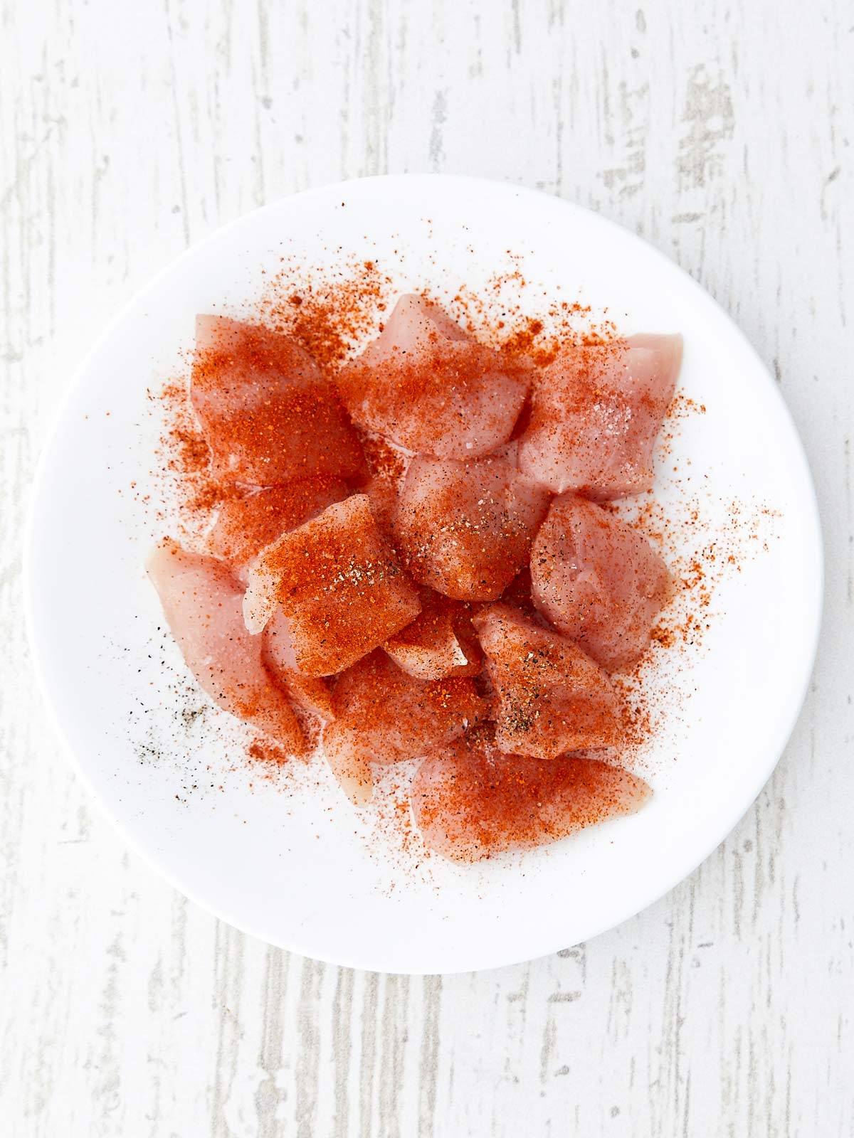Raw chicken cubes on plate with Nashville Hot Chicken Seasoning sprinkled on.