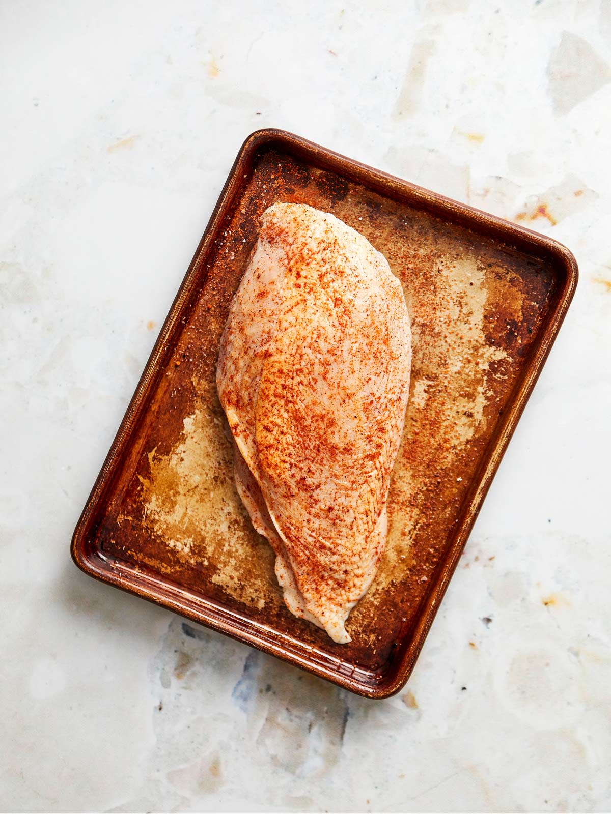 Sheet pan with one seasoned chicken breast.
