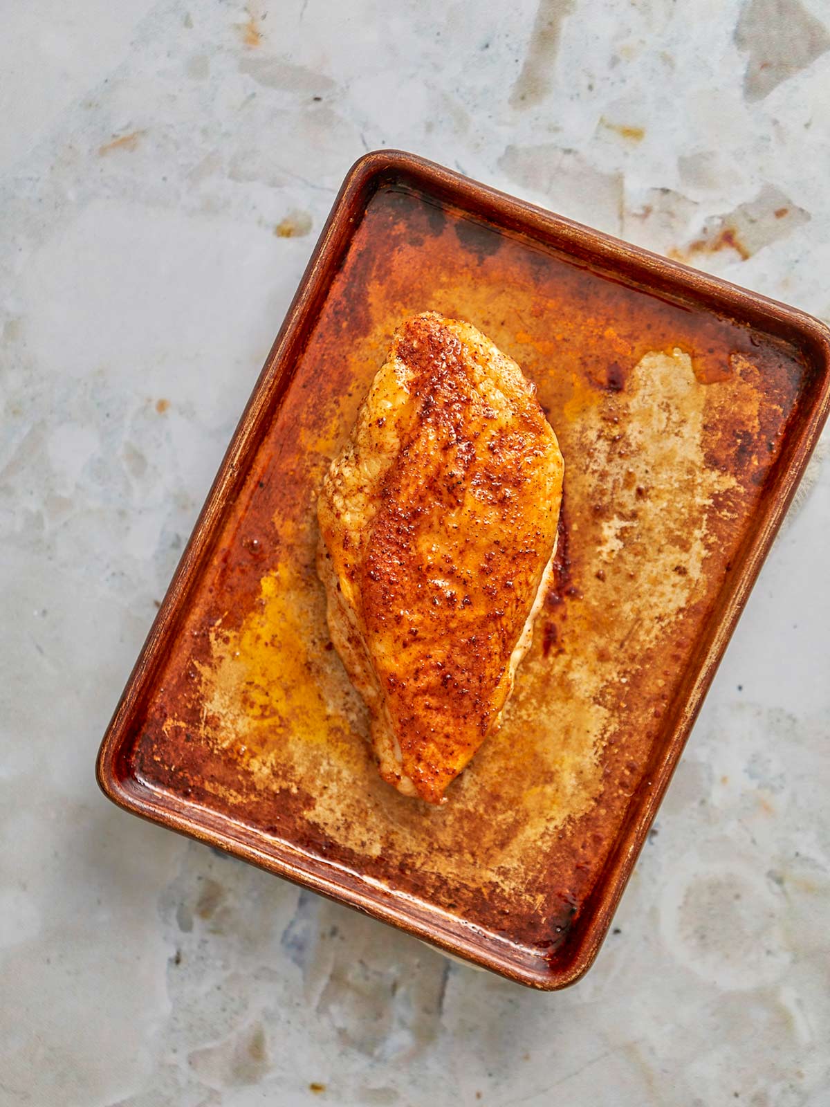 Sheet pan with one baked chicken breast and the juices.