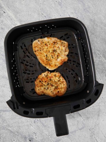 Air fryer basket with two golden brown cooked turkey cutlets.