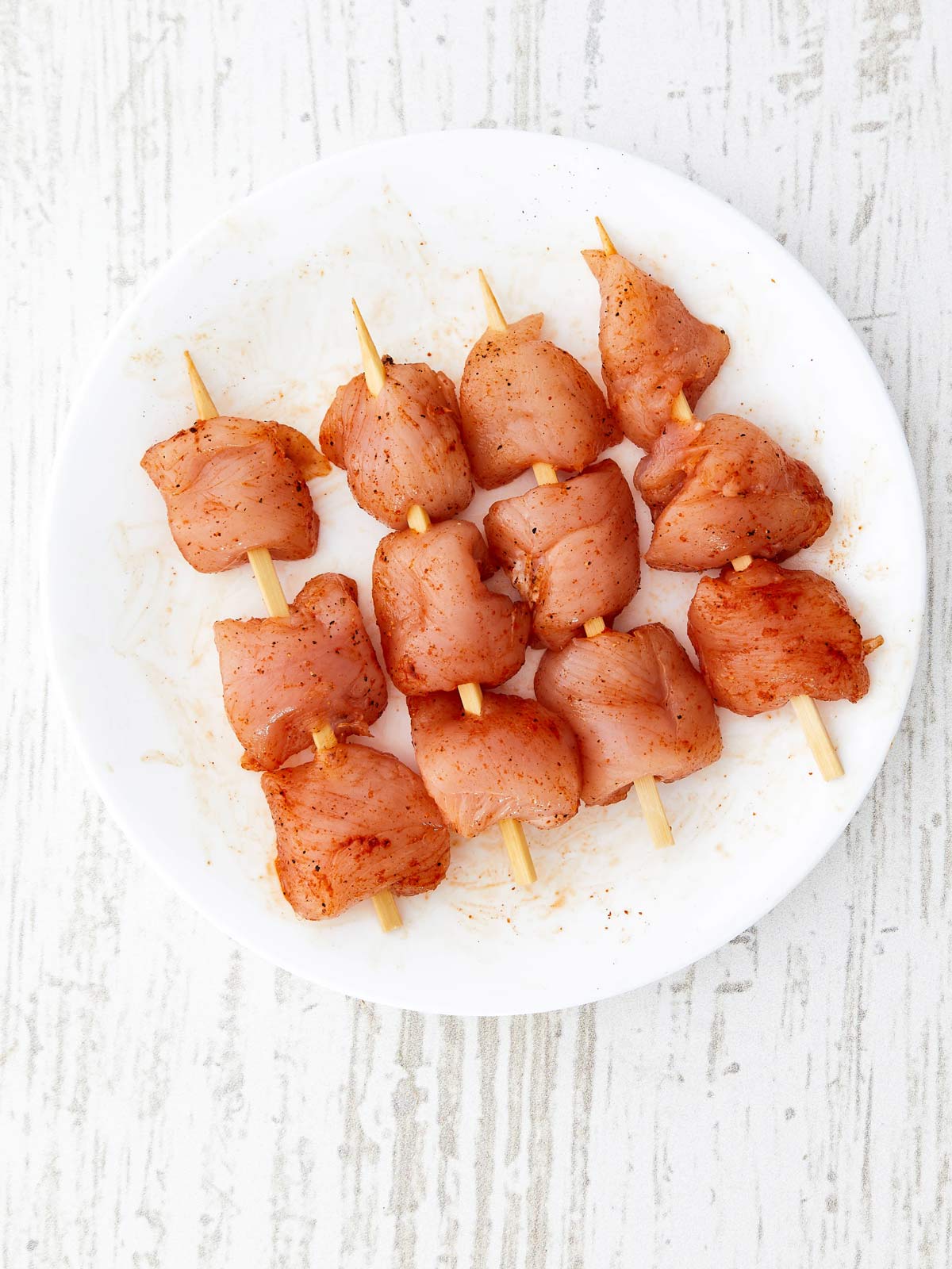 Seasoned raw chicken placed on wooden skewers.
