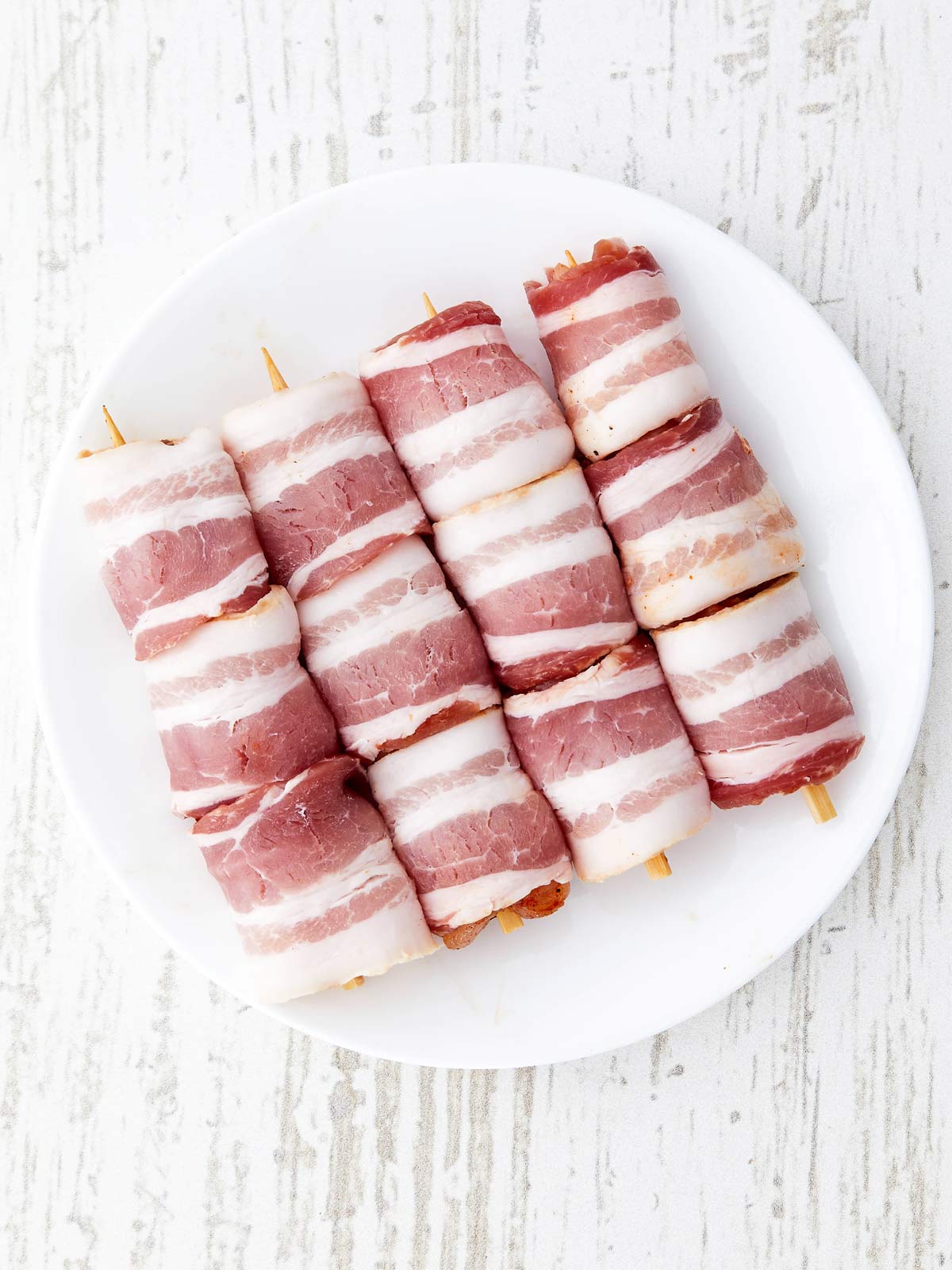 Raw chicken on skewers with raw bacon wrapped around it.